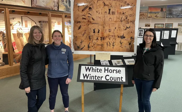Kelly Kirk (left), Director of the Sanford Lab Homestake Visitor Center, along with Emily Berry and Rochelle Zens, who are part of the outreach and culture team at SURF, pose in front of the White Horse Winter Count at the Timber Lake Museum.
