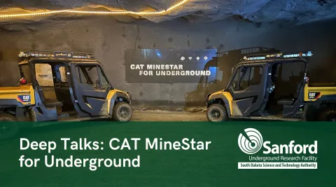 Two side-by-side vehicles are parked on either side of a sign in an underground drift. The sign reads "CAT MineStar for Underground"