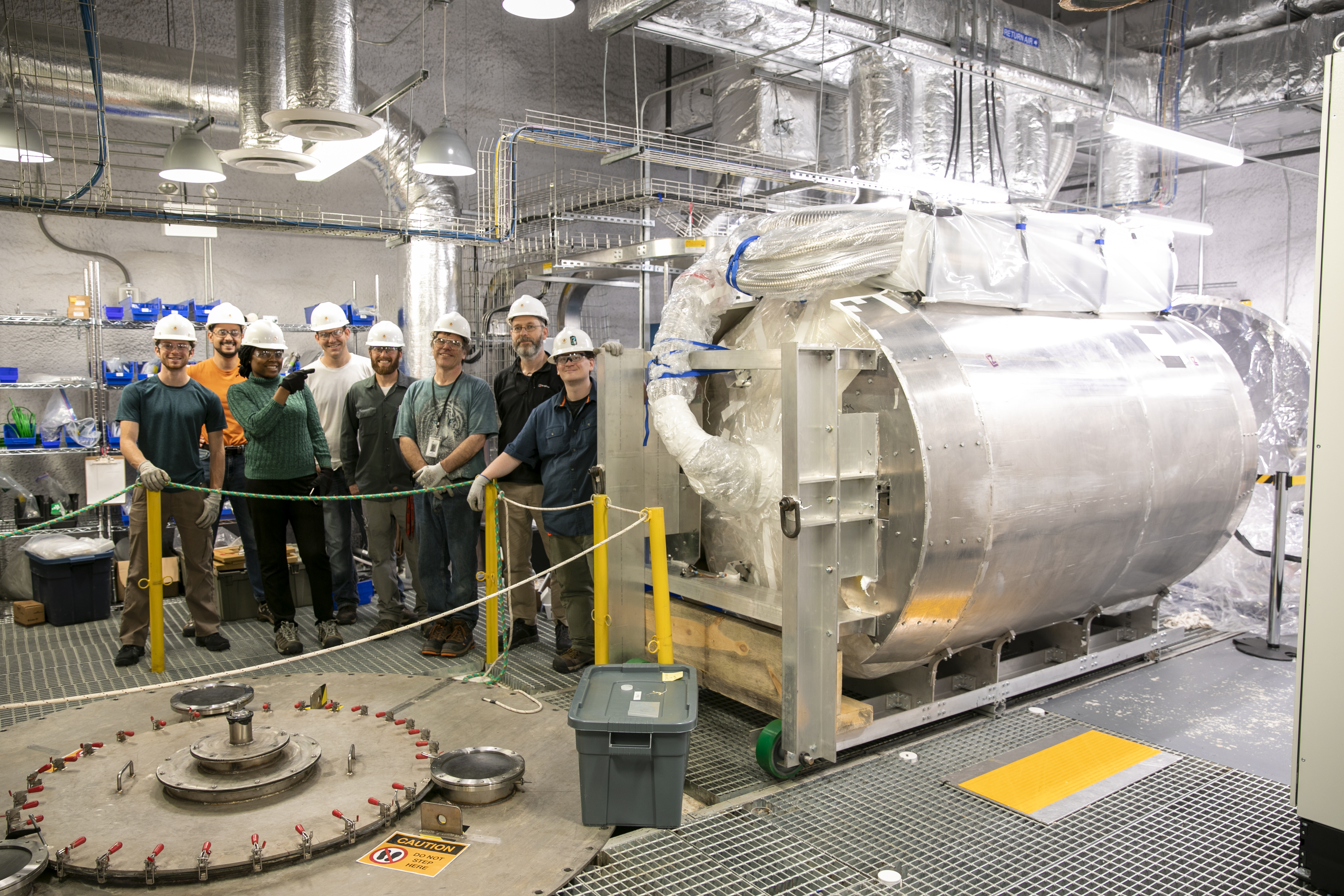 Group of workers stands beside cryostat vessel
