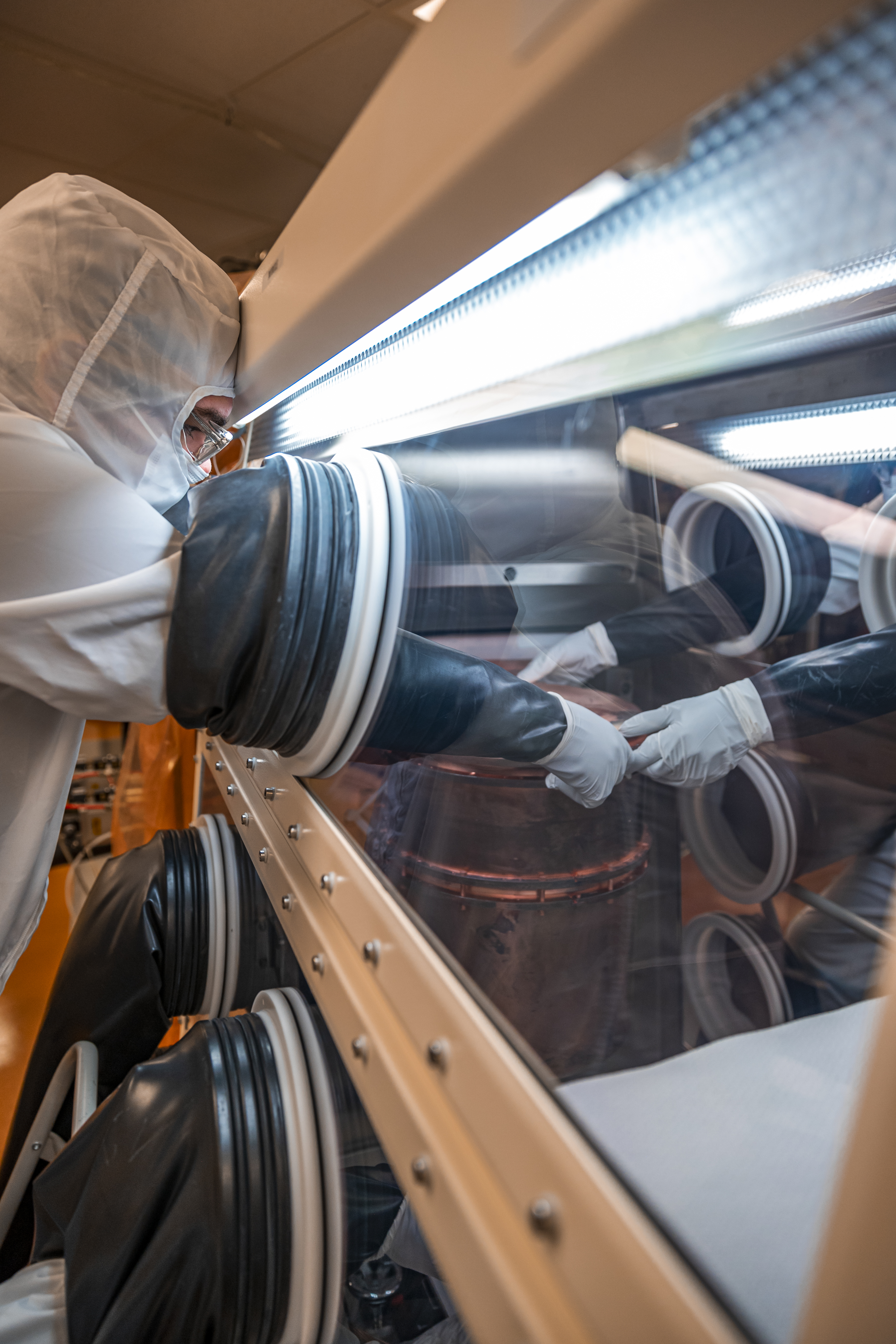 researcher in a clean suit reaches into a glovebox