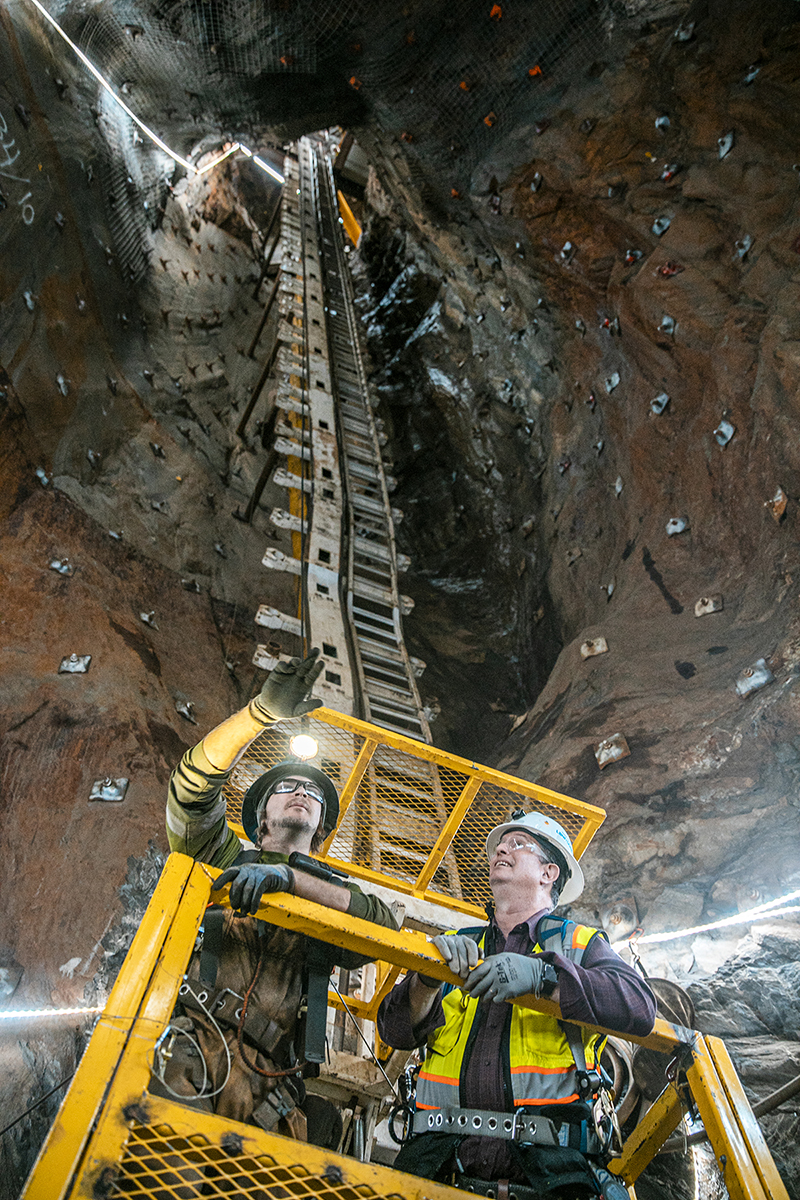 two workers travel down in a cage into the ore pass work area