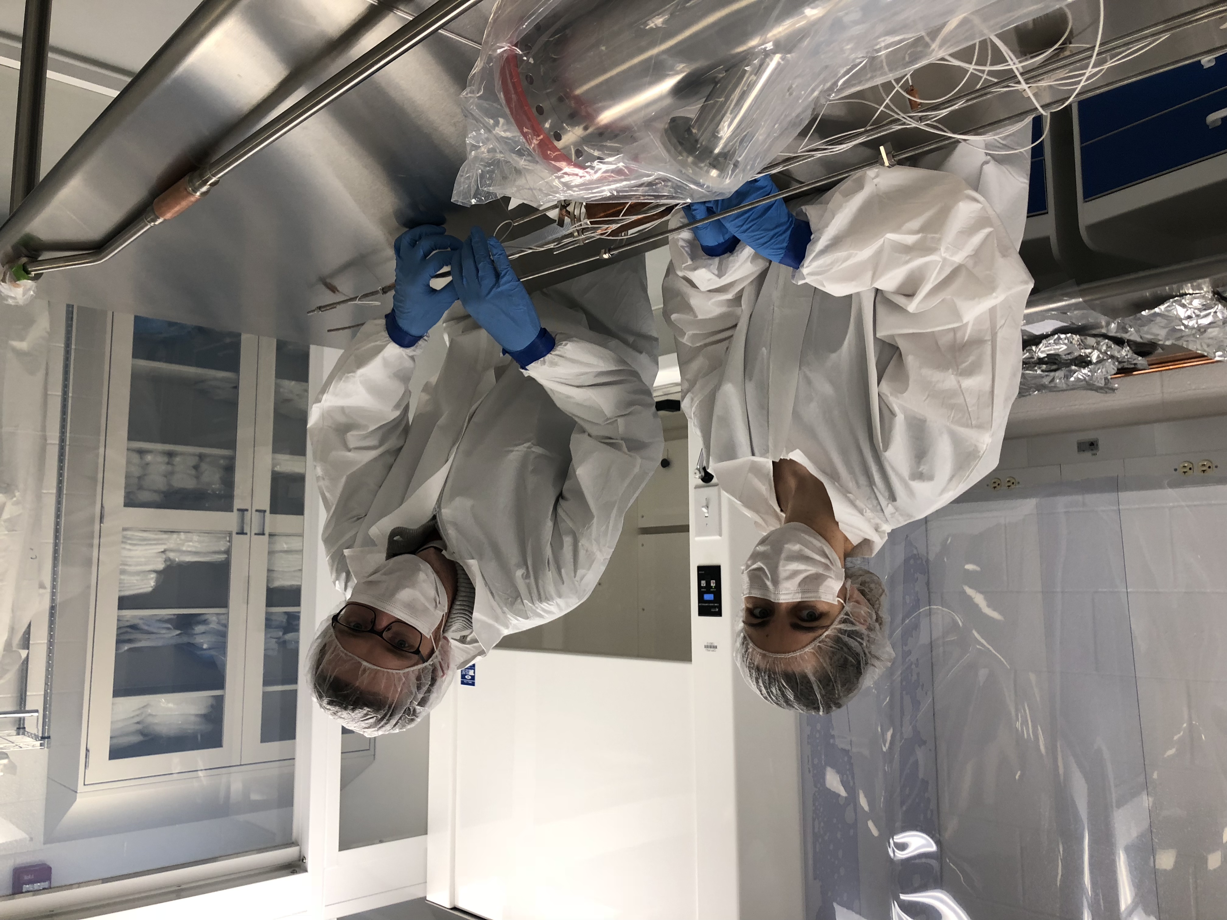 two researchers in clean suits work on experiment components in a cleanroom