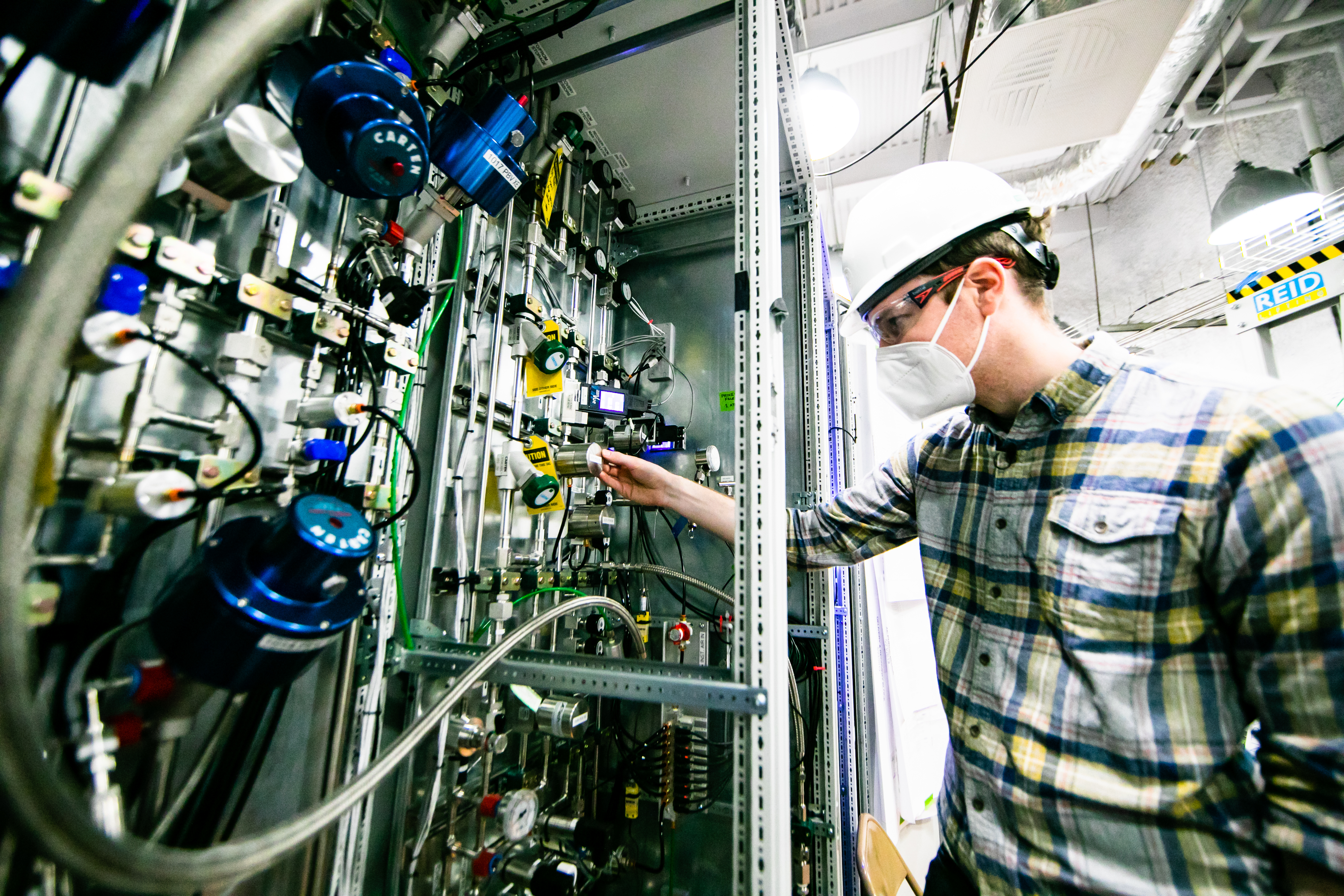 a researcher turns a dial on a complex wall of controls