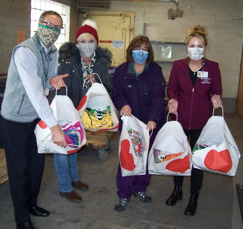 Four people in masks hold bags full of facemasks