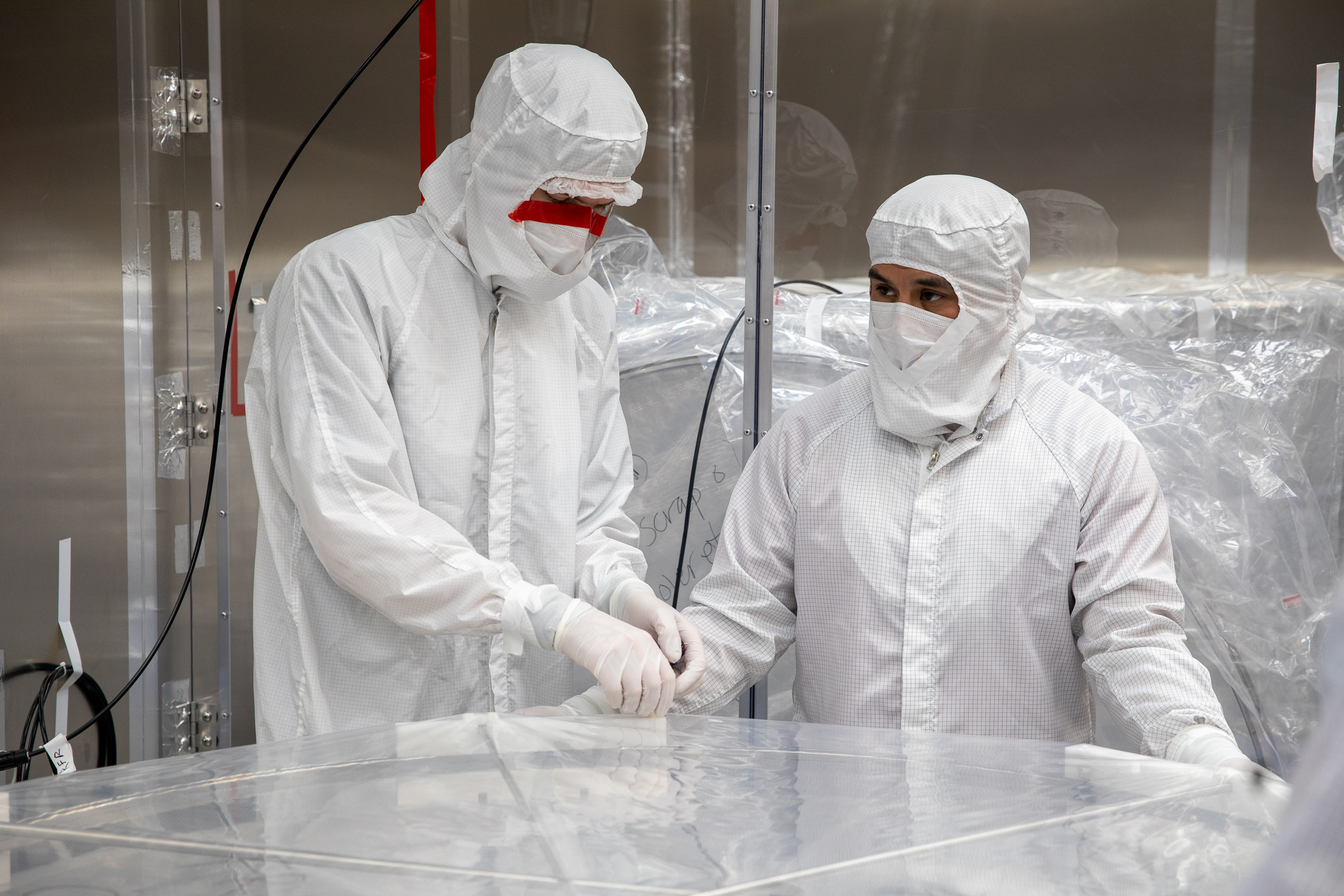 Two people in Tyvek suits stand over an electric grid