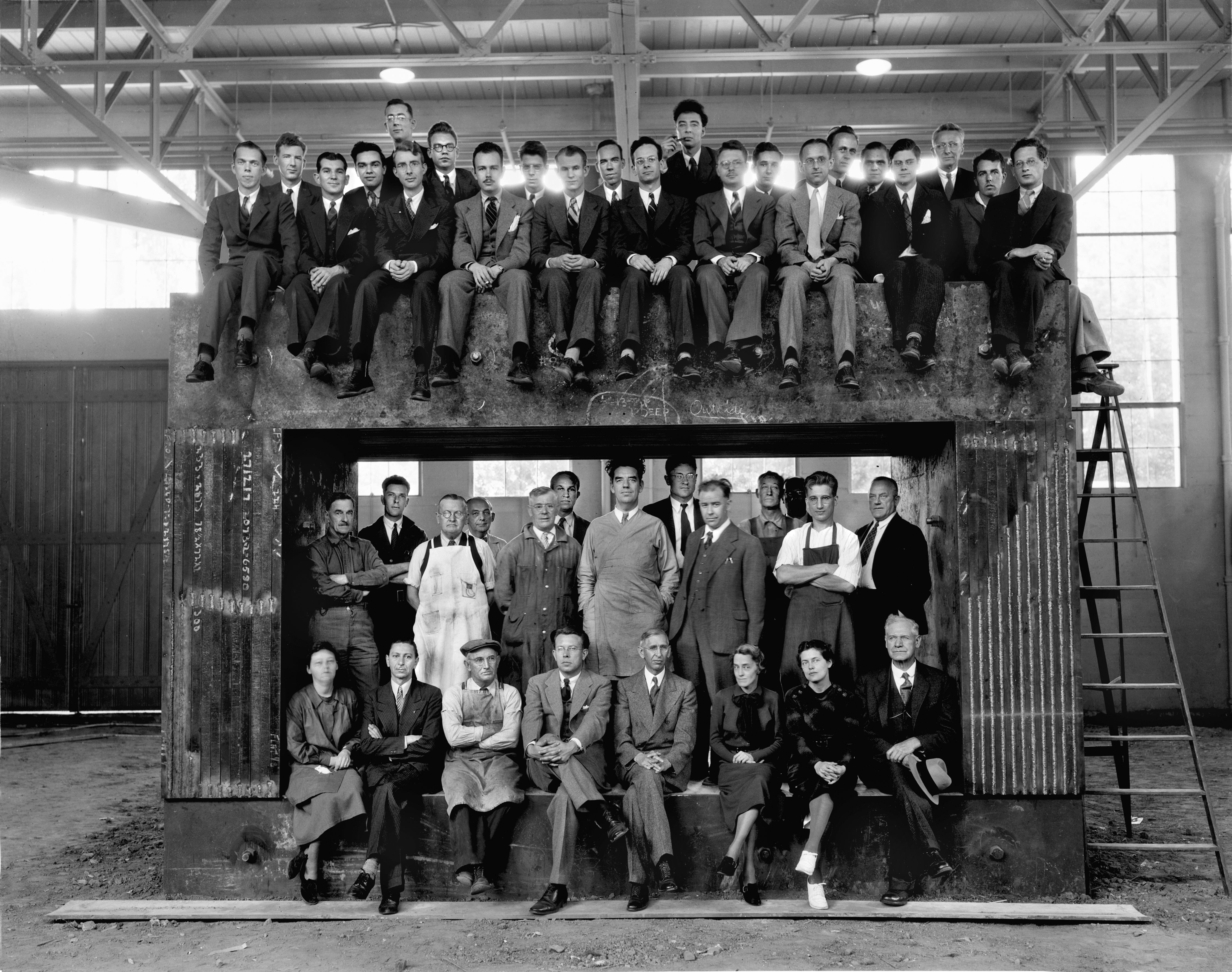 Group of scientists sit on top of a machine, another group stands in front of it