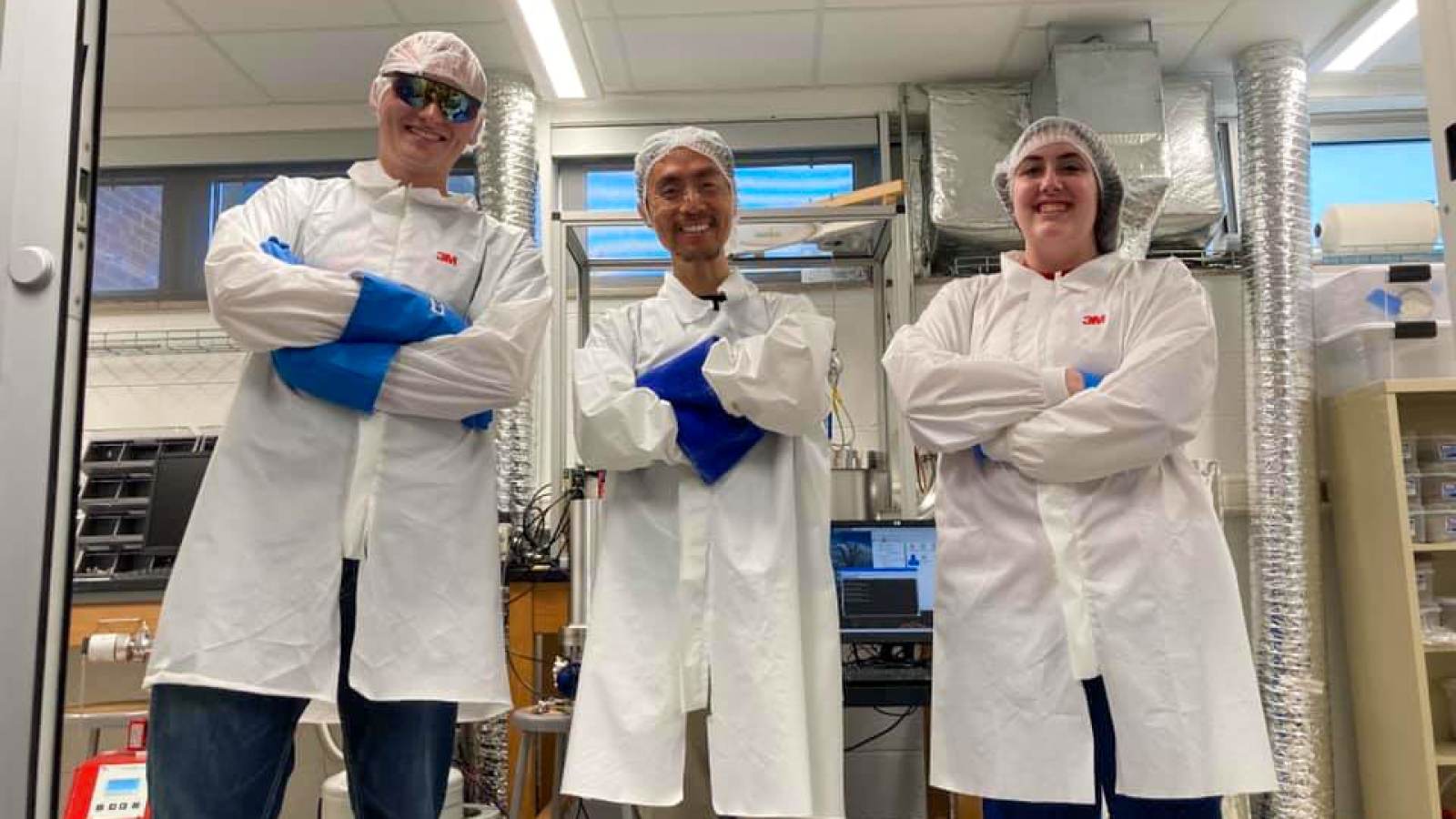 three people stand with their arms crossed in cleanroom suits 
