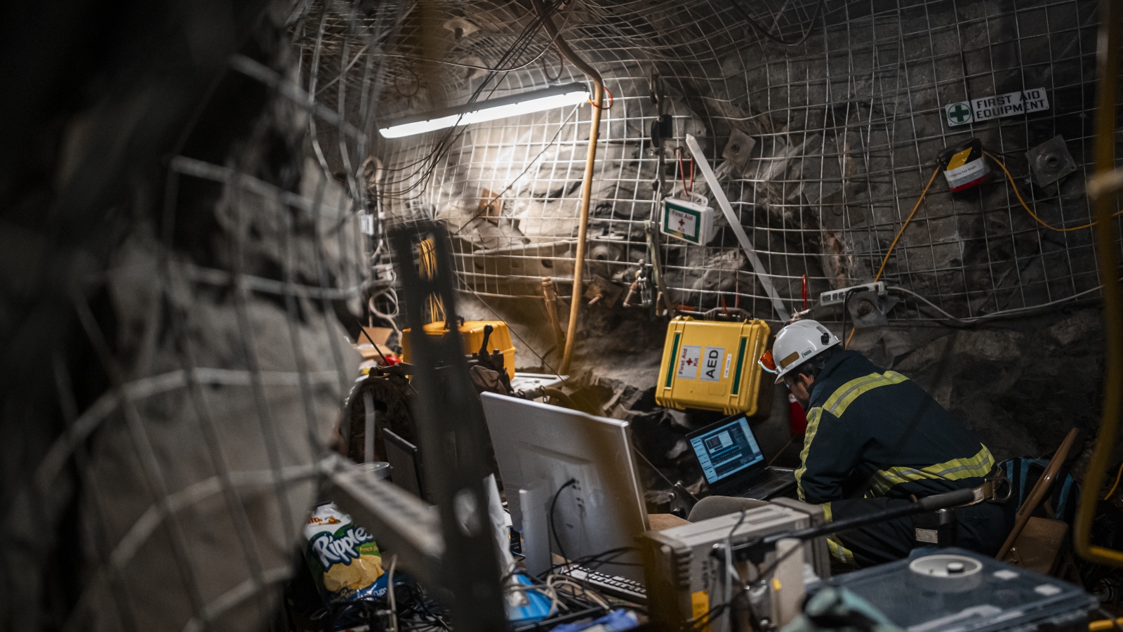 A researcher sits in a drift, looking at a computer. The drift is heavily outfitted with scientific monitoring equipment.