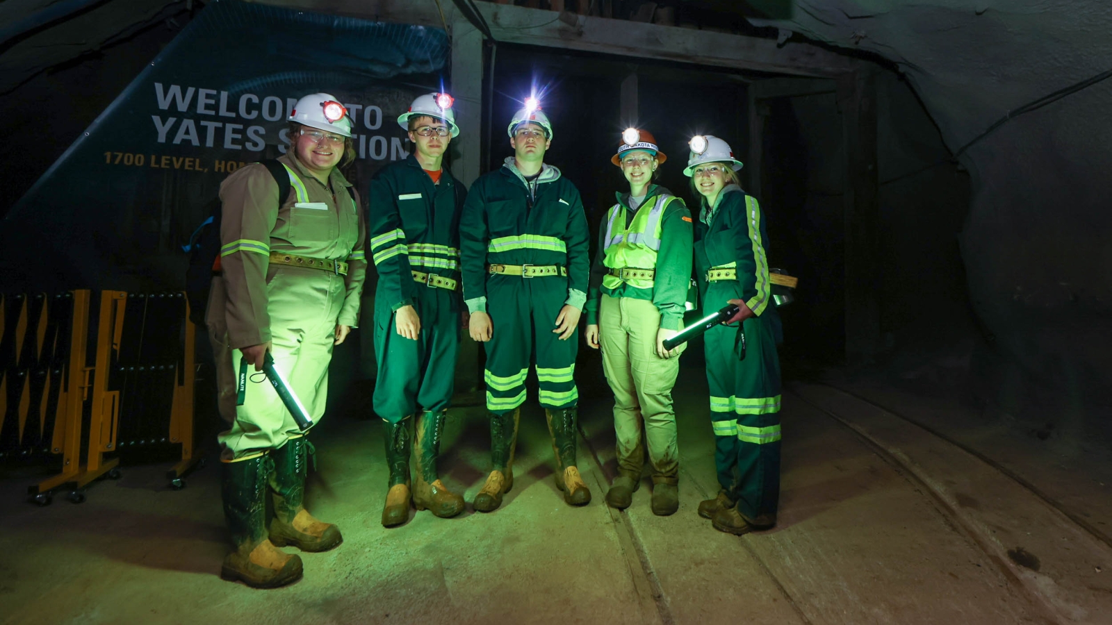 SURF's 2022 summer interns stand in front of the Yates Shaft station, illuminated by green, portable lights 
