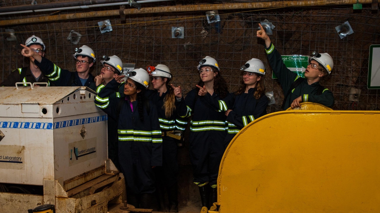 students in underground personal protective equipment stand in a drift and point into the air