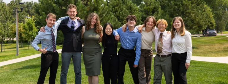 The 2024 Davis-Bahcall Scholars include: (L-R) Colby Routh, Beck Bruch, Nicolette Dame, Huixin Zhang, James Roth, Mackenzie Hollenbeck, Jing Yan, and  Ashley Tieszen - standing on green grass outside dressed up for their presentations.  