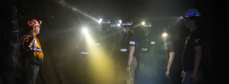 Students taking part in an underground mine rescue simulation wearing  lights and PPE in a darkened cavern. 