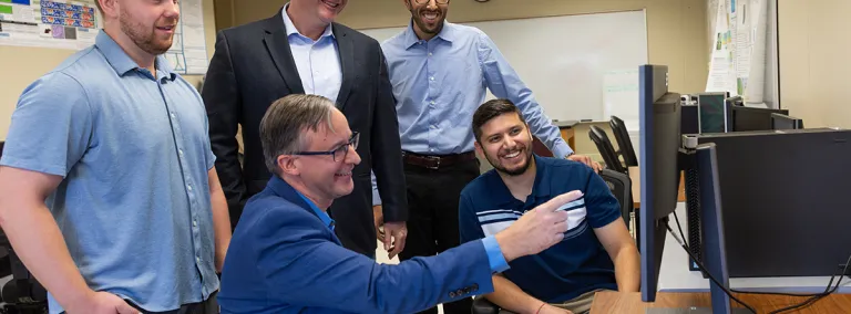 The team at SDSU working on DUNE argon modeling stands around a computer commonly used to process data, those pictured include Vishnu Pfeiffer (M.S. student), Dr. Stephen Gent (Professor), Dr. Gregory Michna (Associate Professor), Sahil Sharma (M.S. student), and Hunter Wallster (M.S. student).  