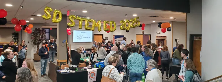 A shot of the balloon sign for the SD STEM ED conference with a room full of people