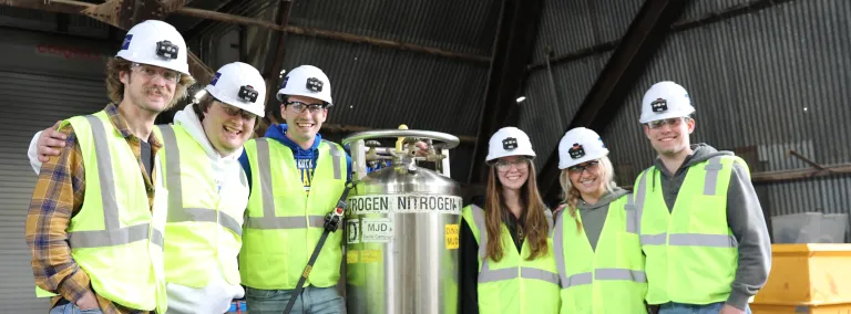 South Dakota State University engineering students in PPE pose around the cart they built to haul liquid nitrogen underground.