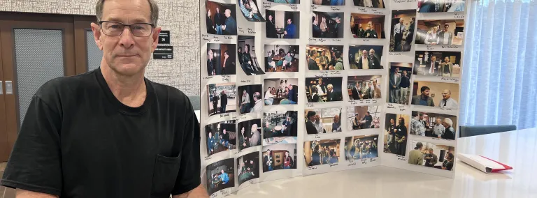 Dale Carter, a Lead, SD area photographer, stands next to a poster board full of photos he has captured of physicists who come to the Black Hills.