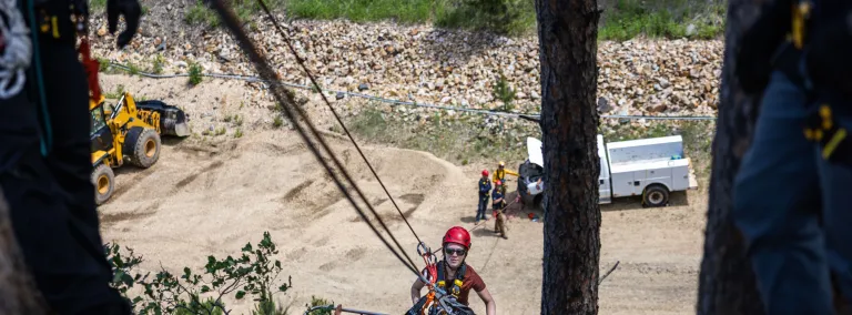 A person on a steep slope in full PPE tied into a set of ropes helping hoist up a stretcher during rescue training at SURF.