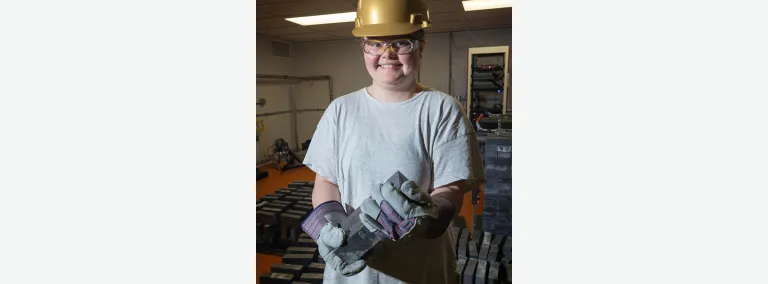 Katie Pedneau poses inside the BHUC holding a brick of led in PPE
