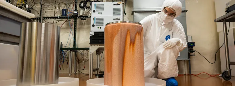 A researcher, in clean-room garb, with a copper mandrel inside the electroforming lab at SURF.