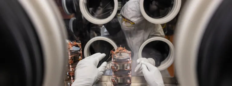 Researchers disassemble components of the MAJORANA DEMONSTRATOR inside a purged glove box in clean room garb. 