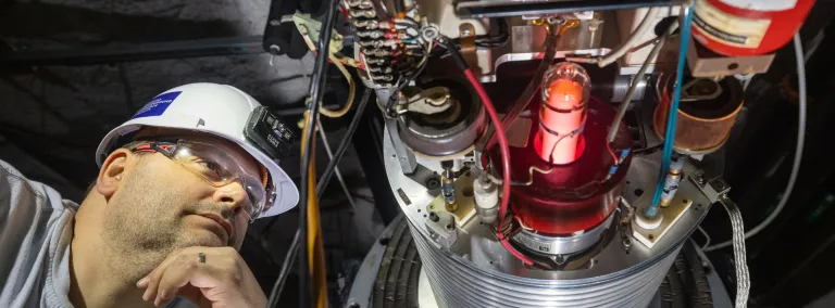 Dan Robertson looks at the plasma container for CASPAR where the beam originates--he's wearing a hard hat and PPE. .
