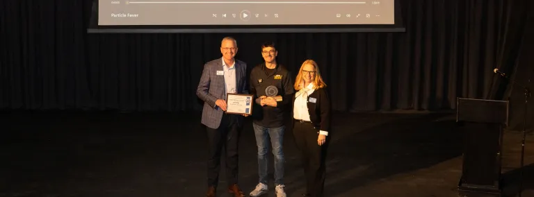 Mike Headley, Todd Jones, and Ann Metli stand on the stage of the Homestake Opera House with the 2025 CORES Award. 