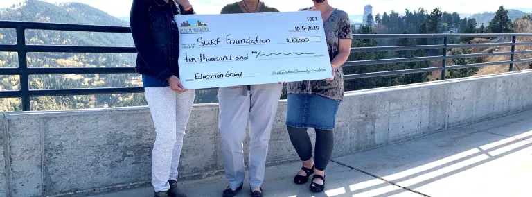 Three people stand on a sidewalk with a giant check 