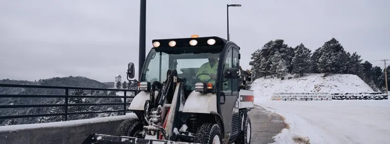 Worker operates a bobcat to remove snow from the parking lot