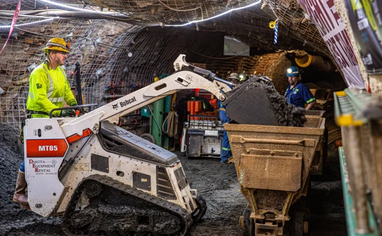 man operates skid steer and dumps rock into ore cart