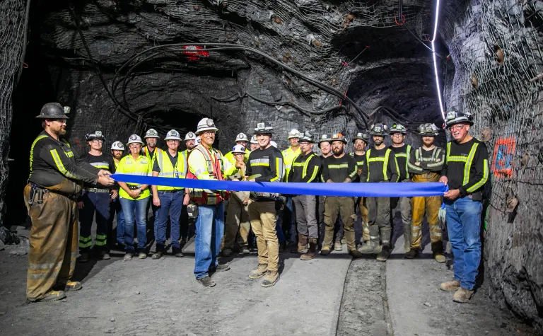 A group of poeple stands in a newly excivated drift a ribbon is being cut with large scissors, everyone is in PPE and smiling.