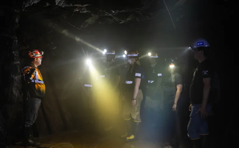 Students taking part in an underground mine rescue simulation wearing  lights and PPE in a darkened cavern. 