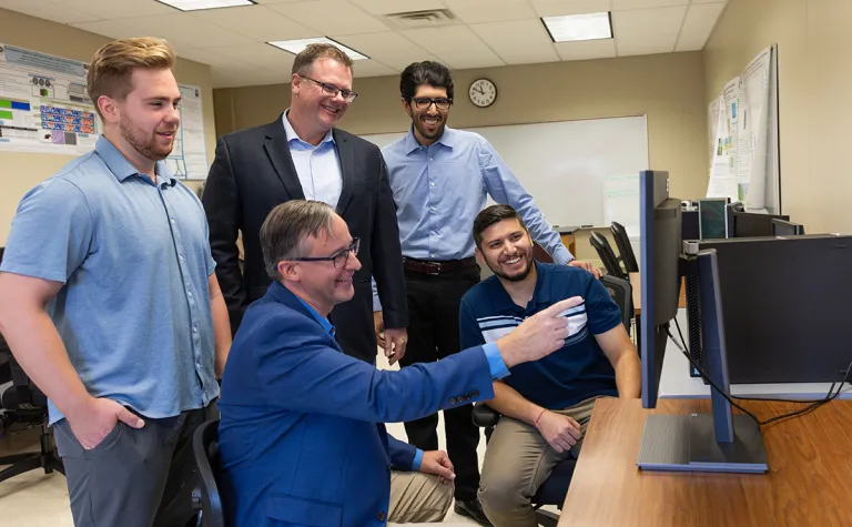 The team at SDSU working on DUNE argon modeling stands around a computer commonly used to process data, those pictured include Vishnu Pfeiffer (M.S. student), Dr. Stephen Gent (Professor), Dr. Gregory Michna (Associate Professor), Sahil Sharma (M.S. student), and Hunter Wallster (M.S. student).  