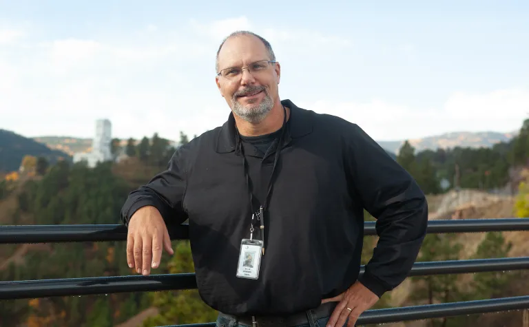 David Rynders poses at SURF near a railing with the Ross Shaft in the background. 