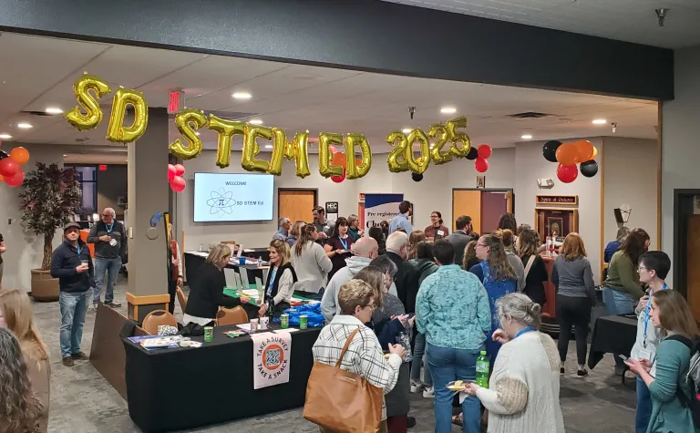 A shot of the balloon sign for the SD STEM ED conference with a room full of people