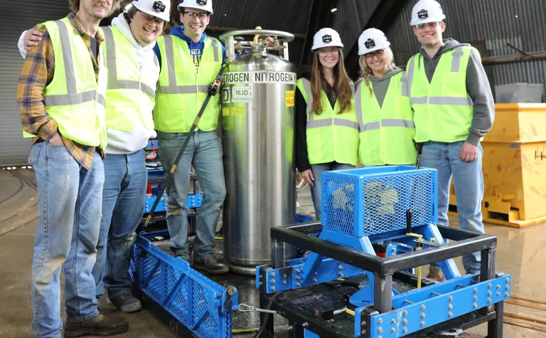 South Dakota State University engineering students in PPE pose around the cart they built to haul liquid nitrogen underground.