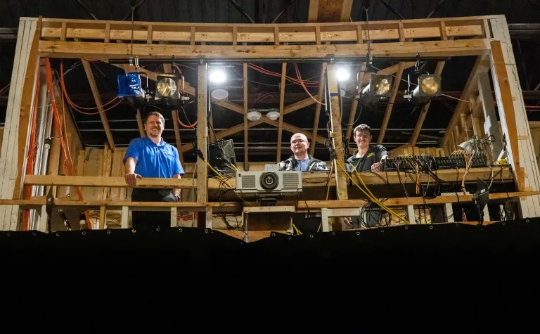 Three people stand in the sound booth at the Homestake Opera House in Lead, the new projector is in the middle of the booth. 