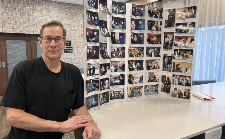 Dale Carter, a Lead, SD area photographer, stands next to a poster board full of photos he has captured of physicists who come to the Black Hills.