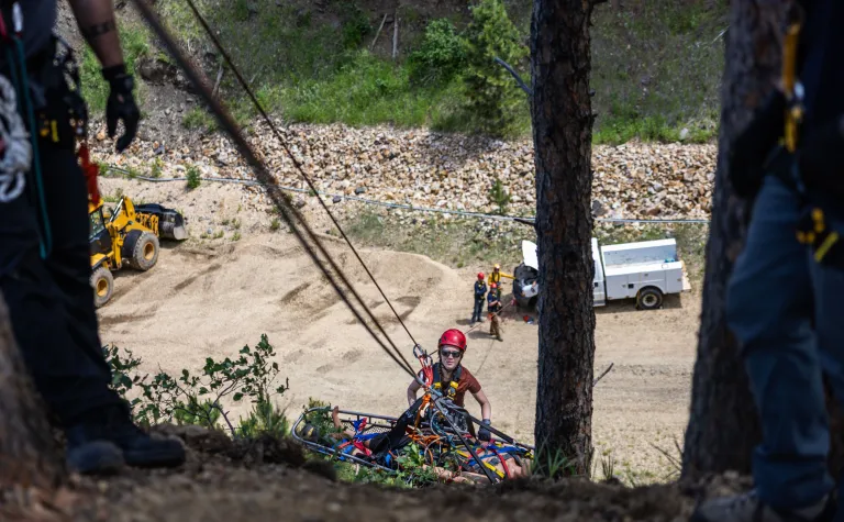 A person on a steep slope in full PPE tied into a set of ropes helping hoist up a stretcher during rescue training at SURF.