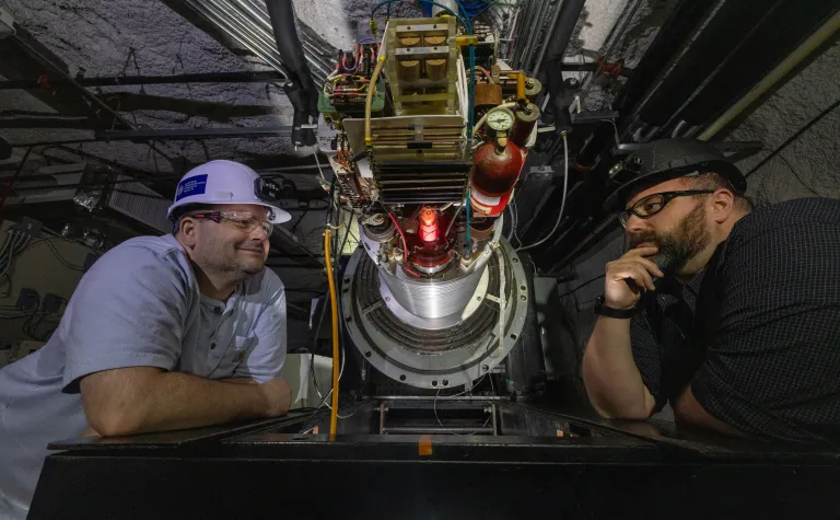 Two researchers on CASPAR stare into the plasma tube inside the accelerator 