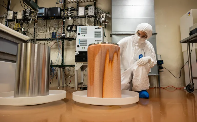 A researcher, in clean-room garb, with a copper mandrel inside the electroforming lab at SURF. 