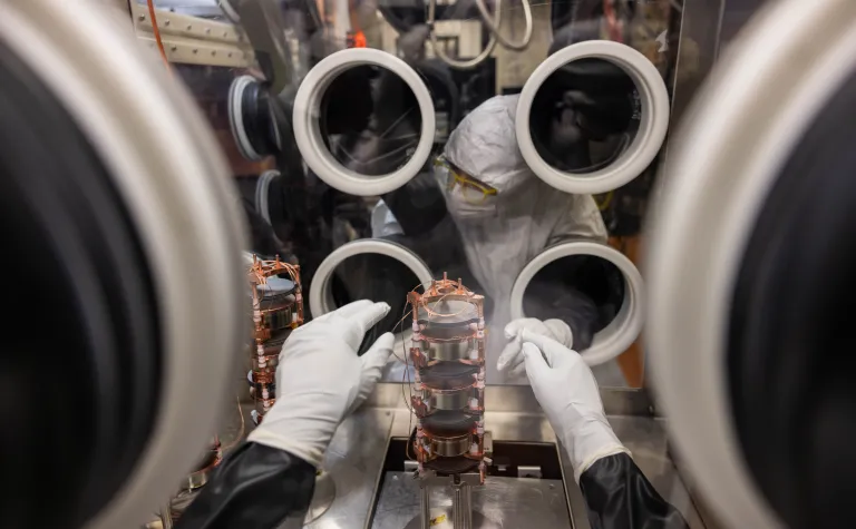 Researchers disassemble components of the MAJORANA DEMONSTRATOR inside a purged glove box in clean room garb. 