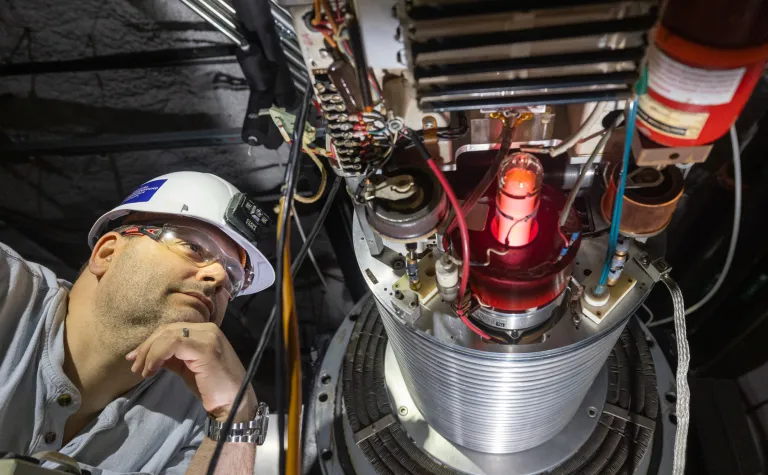 Dan Robertson looks at the plasma container for CASPAR where the beam originates--he's wearing a hard hat and PPE. .