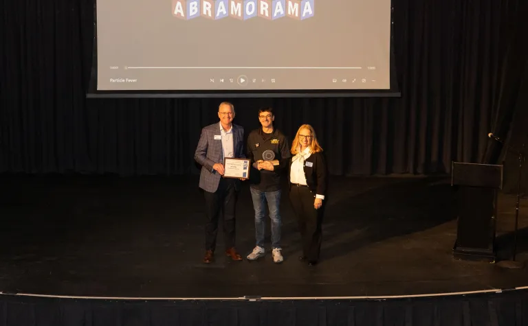 Mike Headley, Todd Jones, and Ann Metli stand on the stage of the Homestake Opera House with the 2025 CORES Award. 