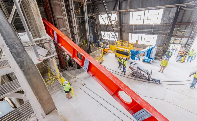 Technicians rig DUNE cryostat beams for loading into the cage--the lift has begun. 