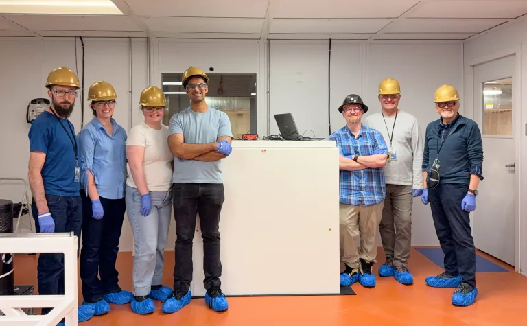 The NEMESIS installation team, (from left) Frederick Shuckman, Brianna Mount, Katie Pedneau, Harkirat Riyat, Doug Tiedt, Alex Barzilov, and Wladyslaw Trzaska stand inside the Black Hills State Underground Campus (BHUC) after the installation of NEMESIS (center). 