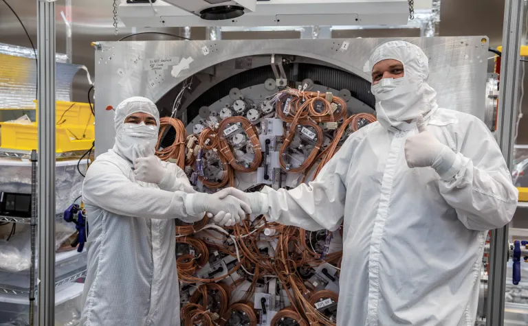 Two people in Tyvek suits shaking hands with thumbs up