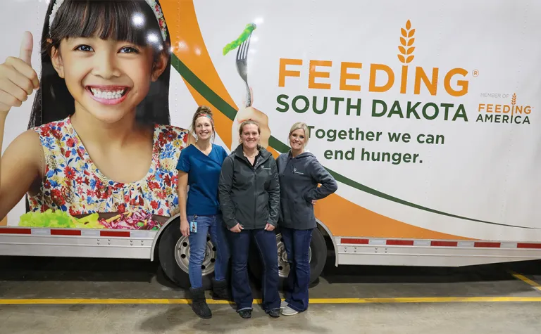 Three people stand in front of the mobile pantry.