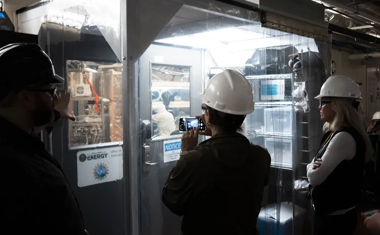 a visitor takes a photo of researchers working inside a cleanroom