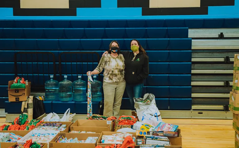 Two people wearing masks stand together in front of holiday gifts for students