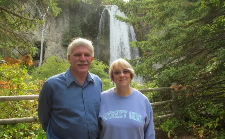 A couple stands in front of a waterfall surrounded by greenery